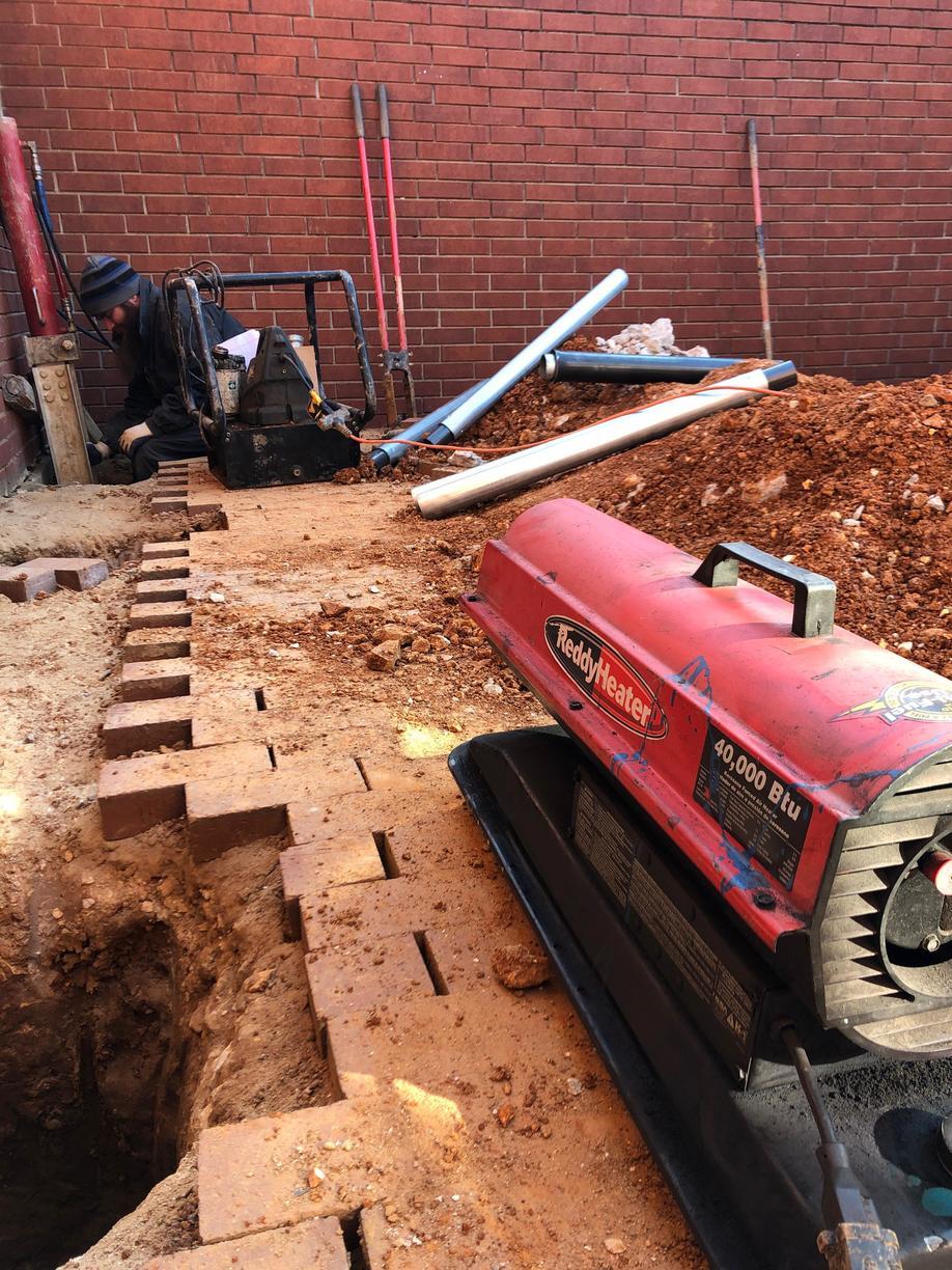 The soil along the foundations edge are removed to install hydraulic driven piers to load bearing soil. This is a picture of Eric working hard to keep piers driving as well as keeping warm!